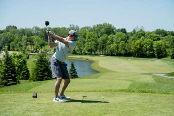 Golfer teeing off, piciture of fairway with trees behind and water on left