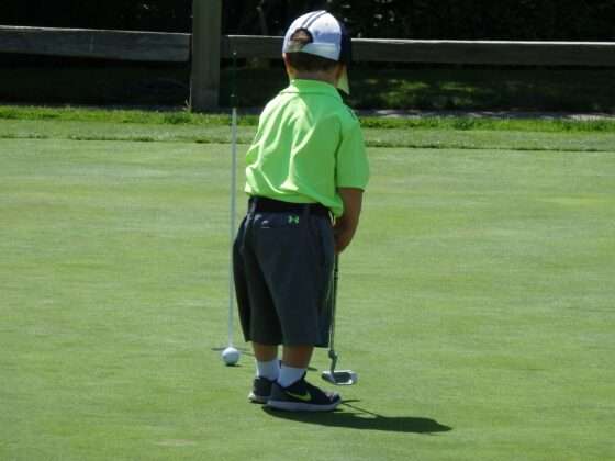 Kid putting on golf green in lime green shirt and oversized hat